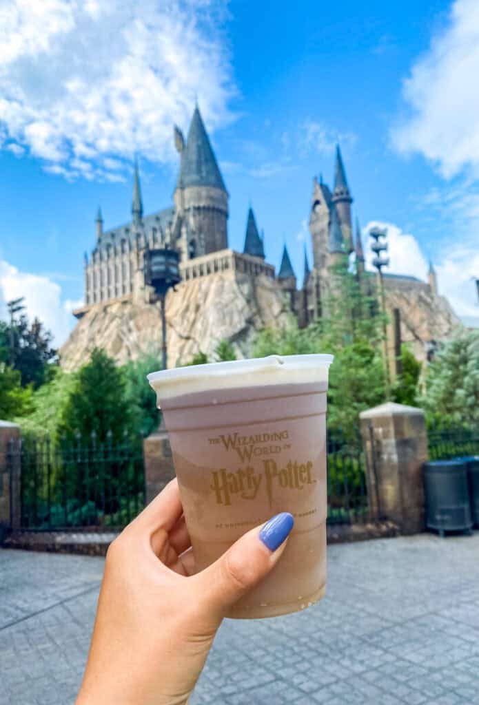 girls hand with blue fingernails holding a cup of Butterbeer in front of the Hogwarts Castle at Harry Potter World Orlando