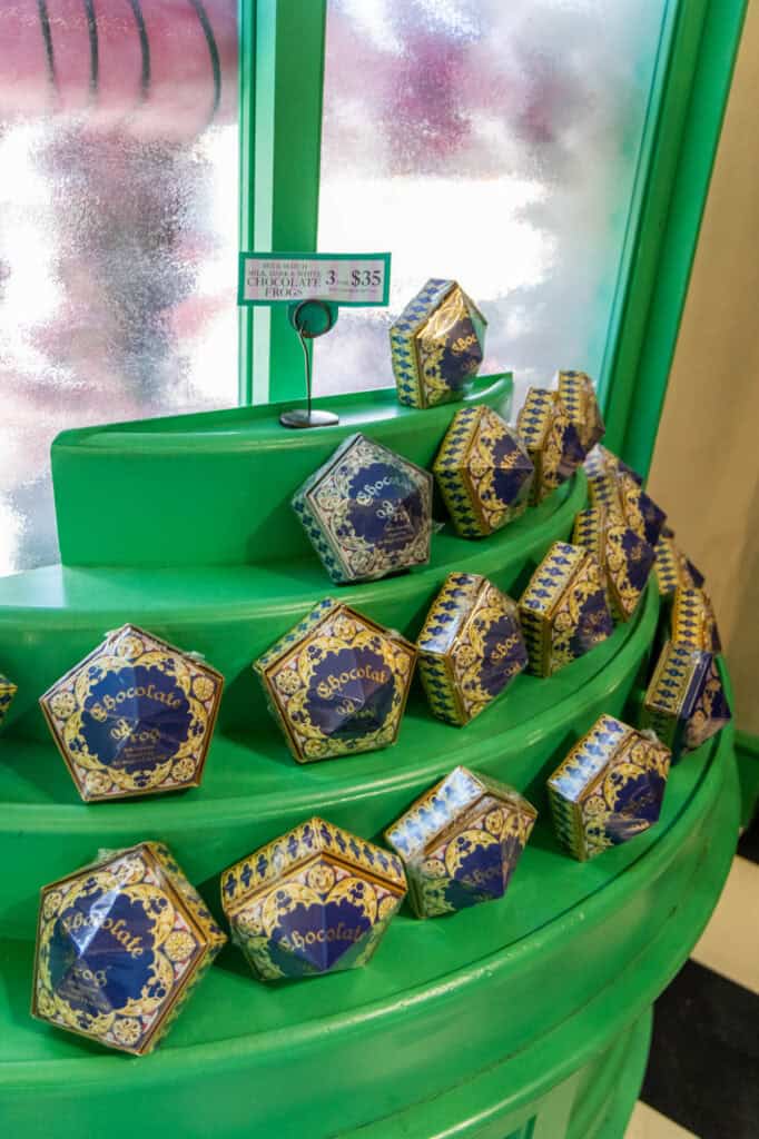A display of iconic Chocolate Frogs in ornate blue and gold packaging sits on a bright green shelf inside a sweets shop at the Wizarding World of Harry Potter. These collectible treats are a fan-favorite souvenir and a whimsical bite of magic you’ll find throughout Harry Potter World.
