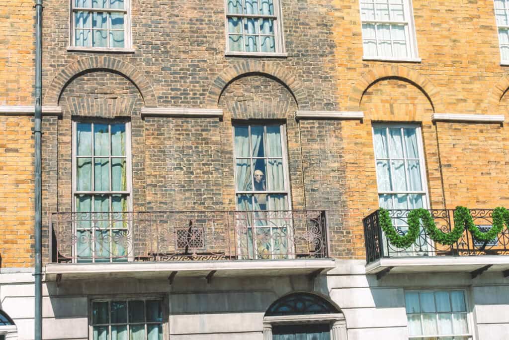 brown and yellow brick buildings with an animatronic house elf peaking through the window. This is the exterior of Grimmauld Place at the Wizarding World of Harry Potter
