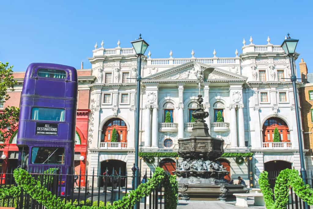 Purple Knight bus and fountain in front of white building facade. This is the entrance to Diagon Alley in Harry Potter World at Universal Studios, Florida