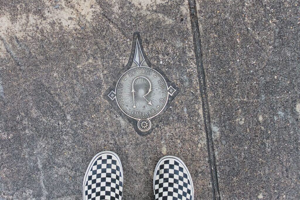 checkered vans shoes below a medallion on the ground. This medallion marks where spells can be cast at Harry Potter World in Orlando, Florida