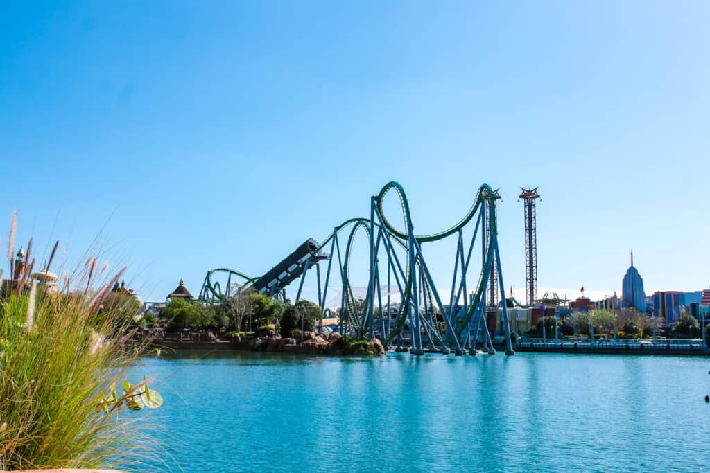Blue lake with shrubbery in foreground and large rollercoaster in the background
