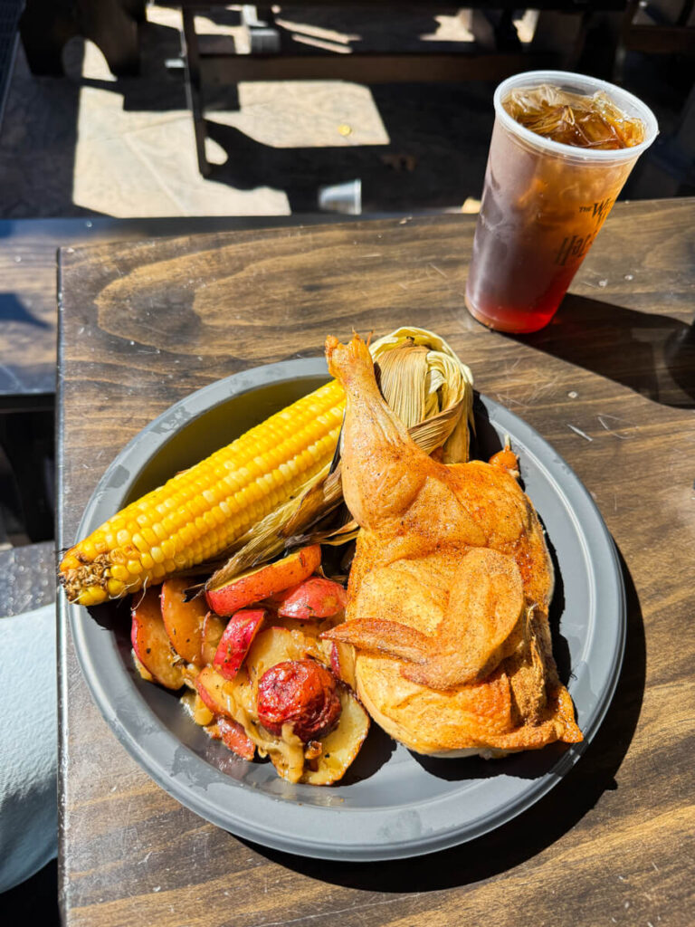 A hearty plate on a rustic table featuring roasted chicken, corn on the cob, and seasoned potatoes, served at the Three Broomsticks in Hogsmeade at Harry Potter World in Islands of Adventure.