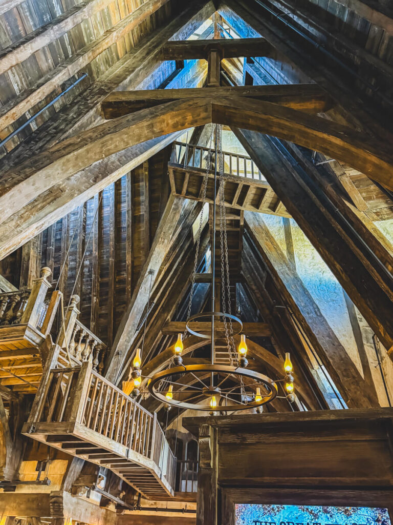 A dramatic view of the vaulted, A-frame ceiling and woodwork inside the Three Broomsticks restaurant at Harry Potter world. Wooden walkways and suspended lights give it a towering, enchanted feel.