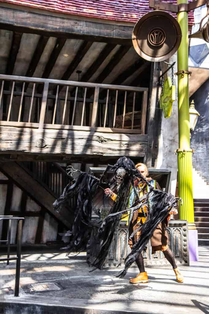 A performer in Diagon Alley at Harry Potter World manipulates a life-sized, tattered puppet of the cloaked figure from The Tales of Beedle the Bard. The shadowy, skeletal character brings a dramatic flair to this live storytelling show, captivating audiences with its haunting presence.