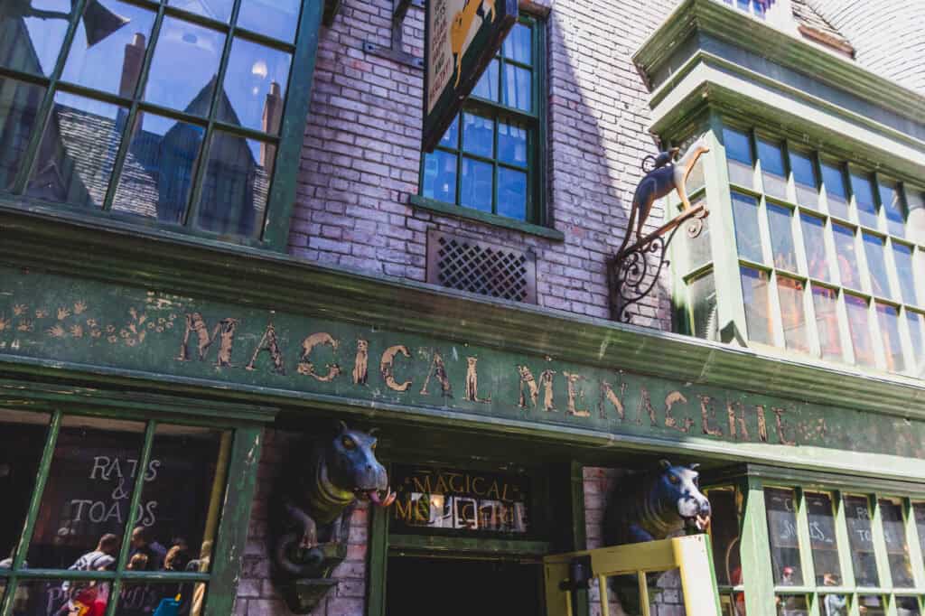 The weathered green facade of the Magical Menagerie shop in Diagon Alley, with painted lettering and whimsical statues of magical creatures flanking the entrance.