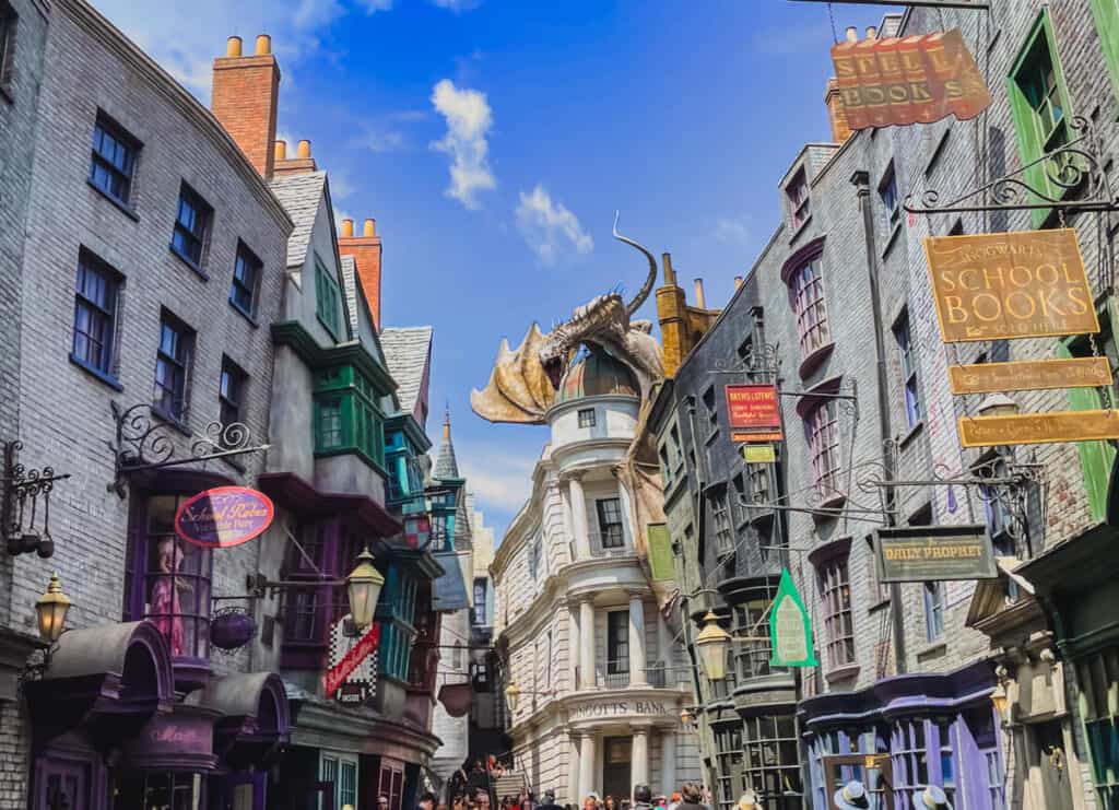 A wide view of Diagon Alley at Universal Studios Florida shows colorful shopfronts, quirky signs like "Daily Prophet" and "Hogwarts School Books," and a dragon perched atop Gringotts Bank. This immersive section of the Wizarding World is a highlight on any Harry Potter World itinerary, capturing the magical atmosphere straight out of the books and films.