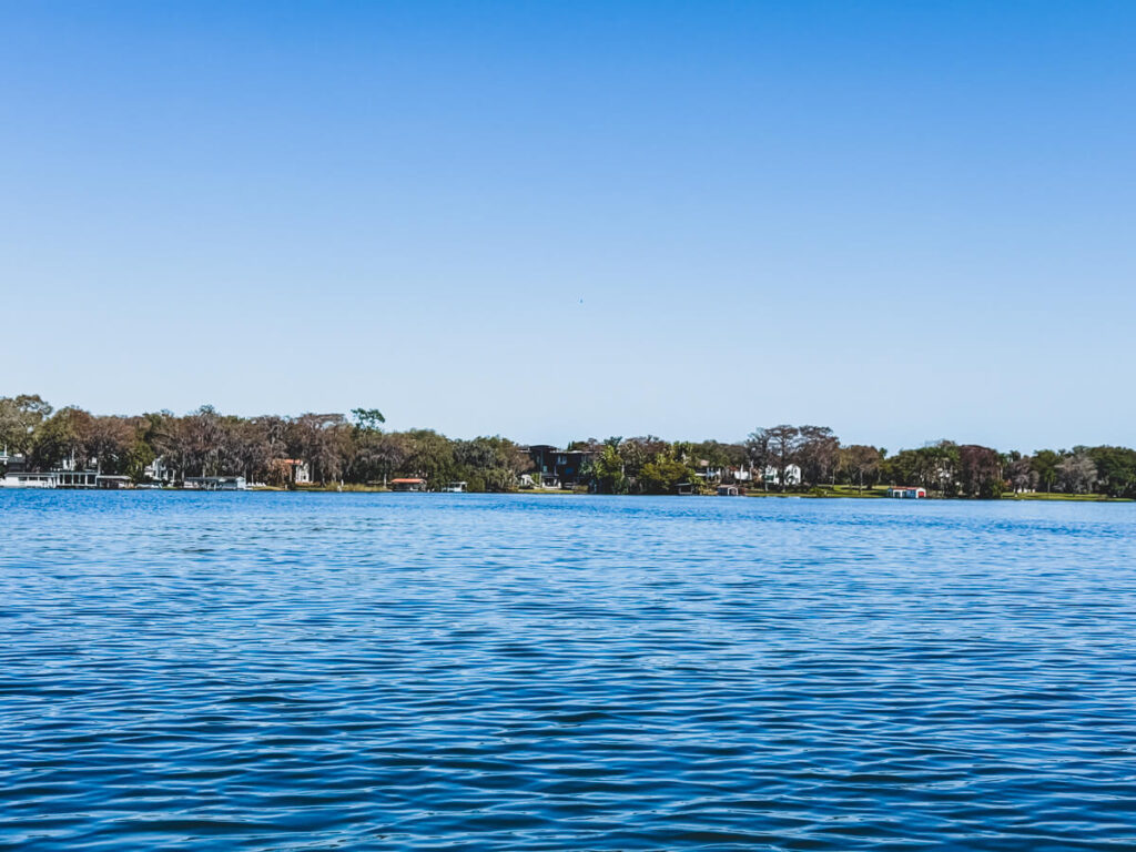 Wide view across Lake Osceola in Winter Park Florida with calm blue water and lakefront homes and trees lining the distant shoreline under a clear sky.