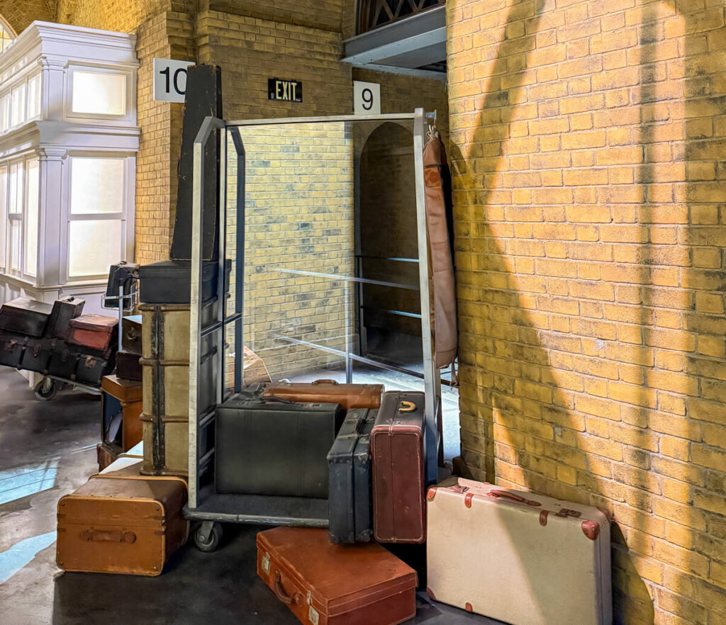 Platform 9 and 3/4 entrance in King's Cross station, with luggage and cart in front of brick wall showing Platforms 9 and 10