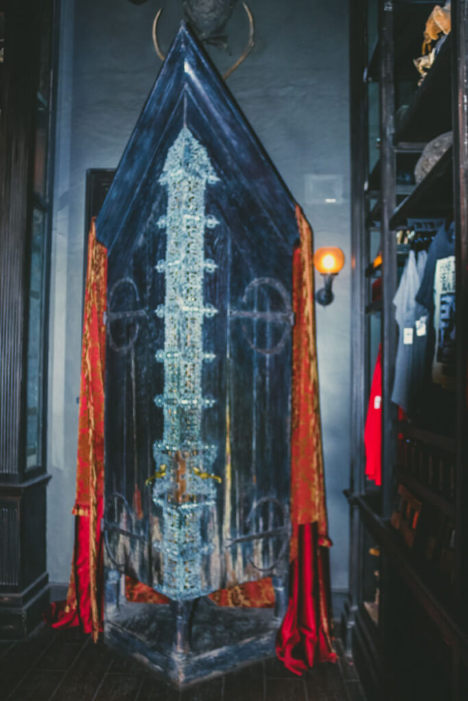 large black cabinet with silver designs and red curtains hanging off the side. This is the Vanishing Cabinet inside of Borgin and Burke's in Diagon Alley