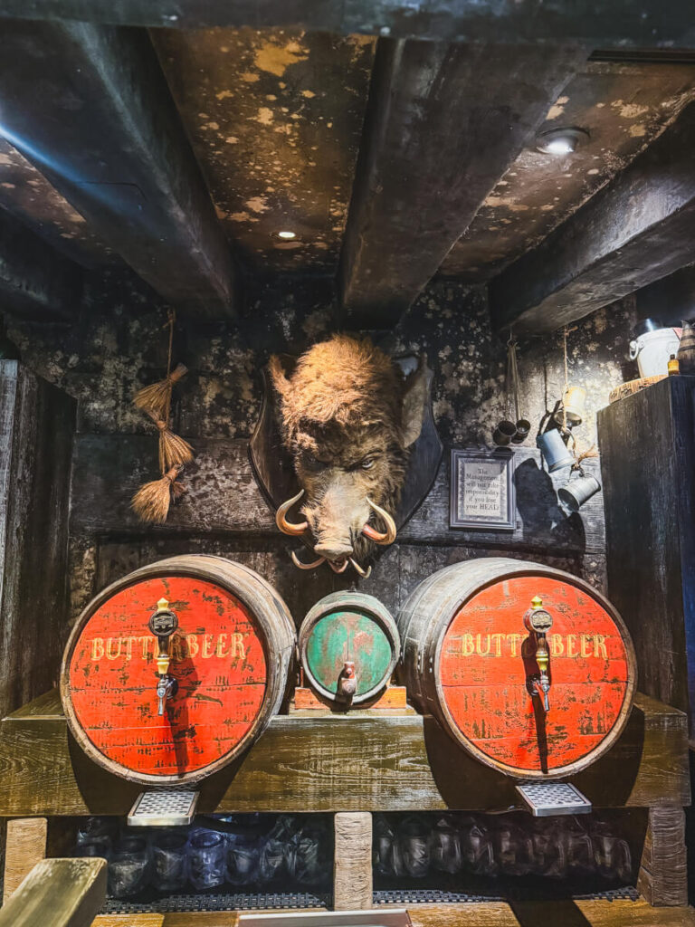 the inside of the Hog's Head pub inside Hogsmeade at Islands of Adventure Florida, including two wall-mounted barrels of Butterbeer, a small barrel in the middle, and a large Hog's head on the wall behind them